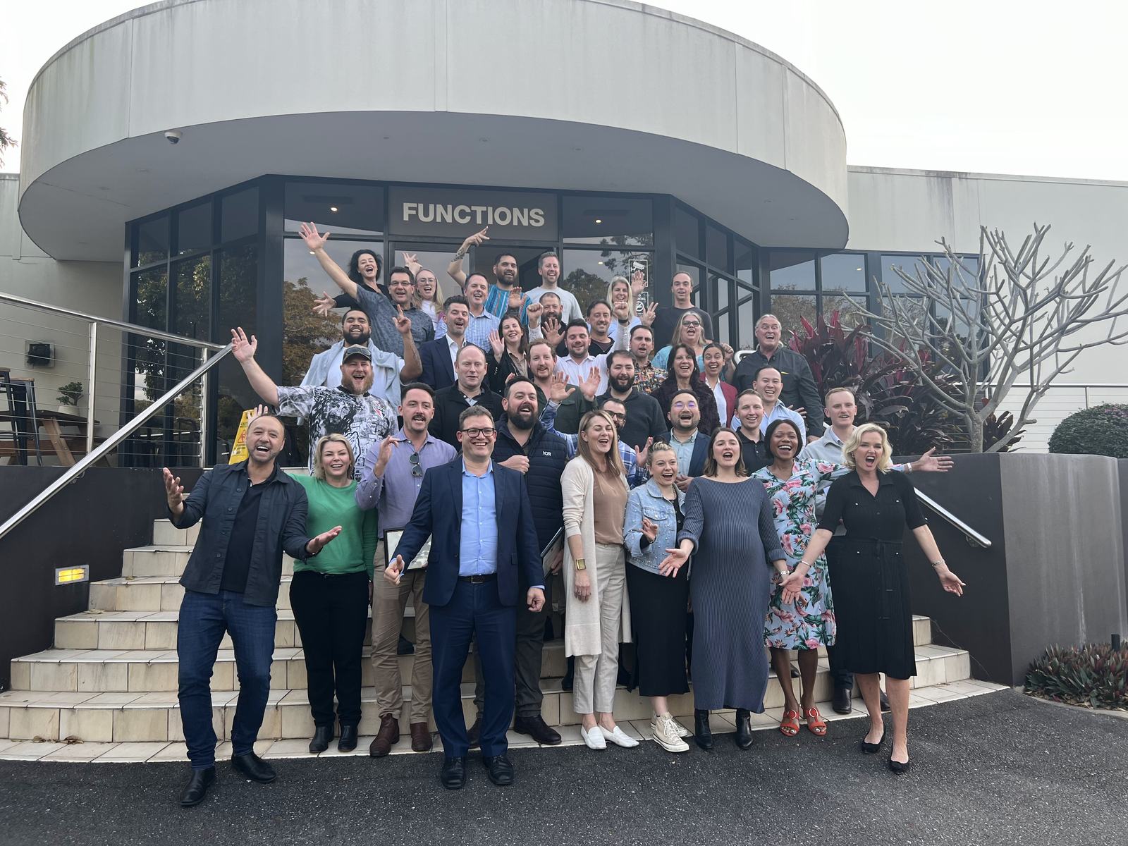 A large Dale Carnegie class cheering with arms raised on the steps outside the Jindalee function centre