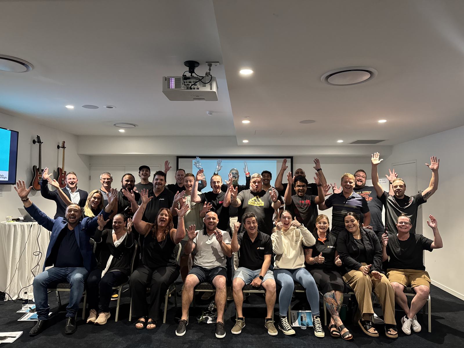 A full Dale Carnegie class seated in rows in a training room, waving at the camera